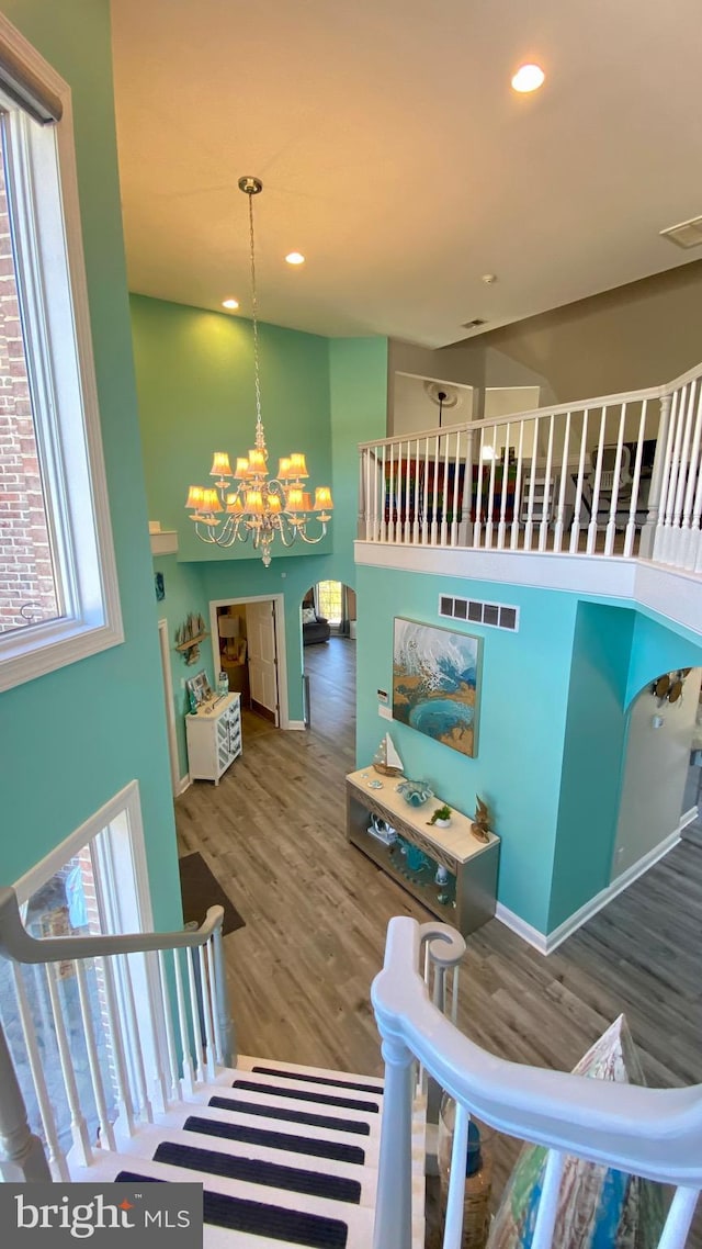 stairway featuring plenty of natural light, wood-type flooring, and an inviting chandelier