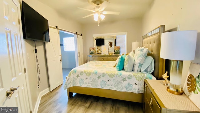 bedroom with a barn door, ceiling fan, and dark wood-type flooring