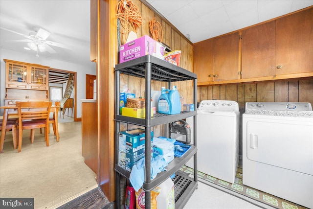 laundry room with wooden walls, independent washer and dryer, cabinets, light colored carpet, and ceiling fan