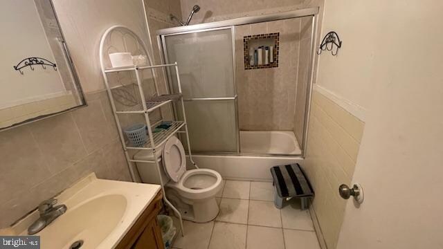 full bathroom featuring vanity, bath / shower combo with glass door, tile patterned floors, toilet, and tile walls