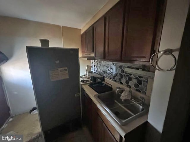 kitchen featuring light countertops, decorative backsplash, a sink, dark brown cabinets, and under cabinet range hood