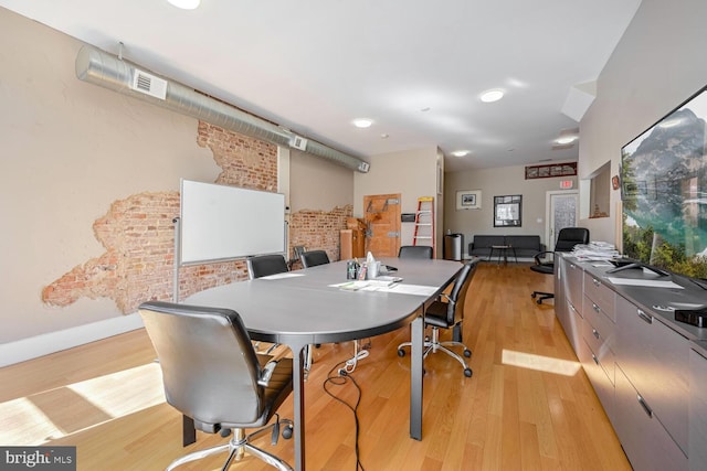 office area featuring light wood-type flooring and brick wall