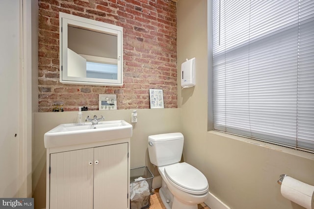 bathroom featuring vanity, toilet, and brick wall