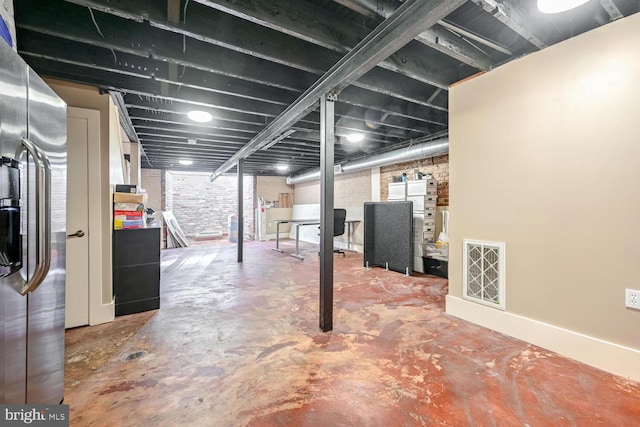 basement with stainless steel refrigerator with ice dispenser and brick wall