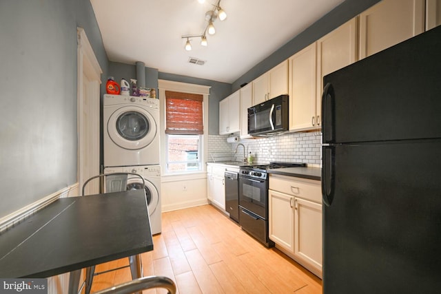 kitchen with light hardwood / wood-style floors, stacked washer and clothes dryer, decorative backsplash, black appliances, and sink