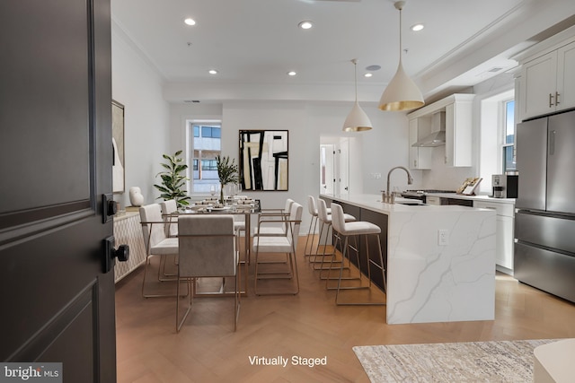 kitchen featuring light parquet flooring, stainless steel fridge, white cabinetry, hanging light fixtures, and an island with sink