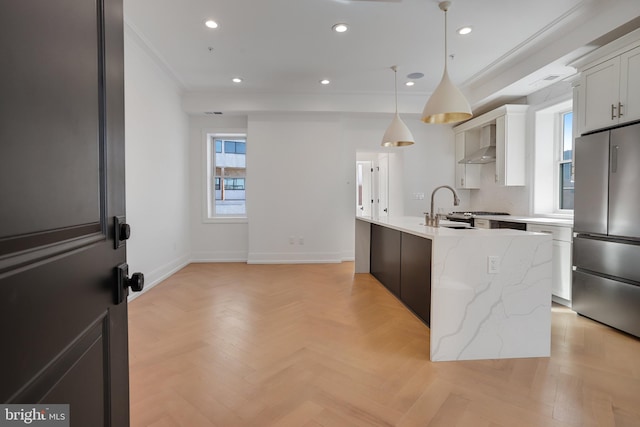 kitchen featuring light stone counters, decorative light fixtures, an island with sink, white cabinets, and stainless steel fridge