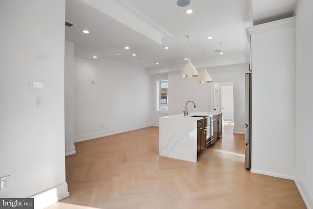 kitchen with light parquet flooring, hanging light fixtures, an island with sink, and light stone countertops