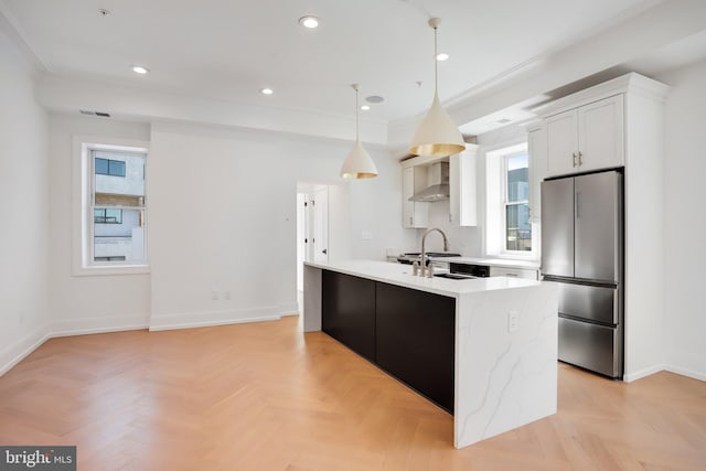 kitchen featuring light parquet flooring, white cabinetry, decorative light fixtures, stainless steel refrigerator, and wall chimney exhaust hood