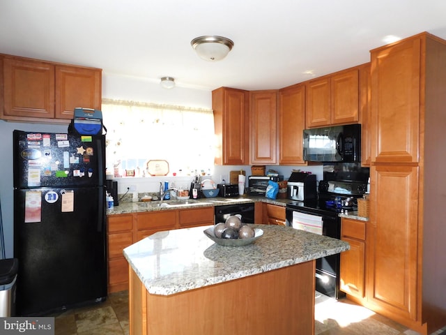 kitchen with sink, black appliances, light stone counters, and a center island