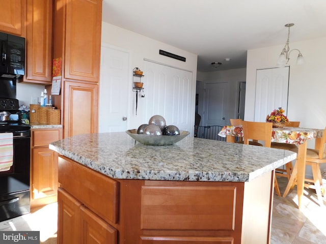 kitchen featuring black appliances, pendant lighting, light stone counters, and a center island