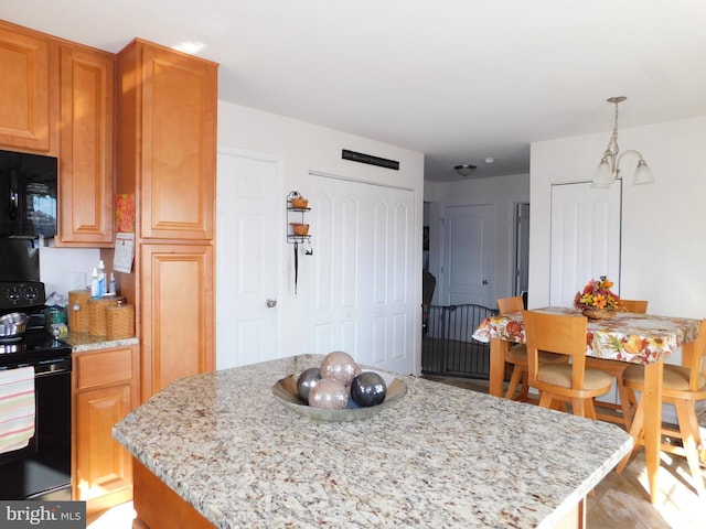 kitchen featuring pendant lighting, black appliances, light stone counters, and a center island