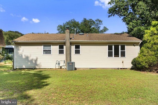 rear view of property with central air condition unit and a lawn