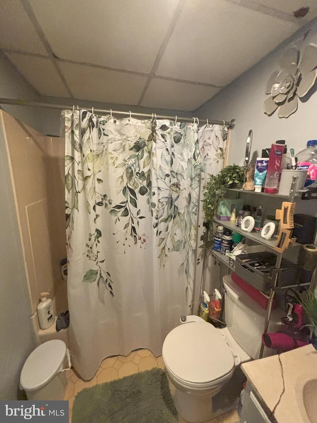 bathroom with toilet, vanity, a drop ceiling, and a shower with shower curtain