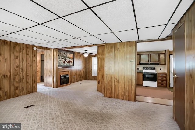 unfurnished living room featuring a drop ceiling, wood walls, ceiling fan, and heating unit