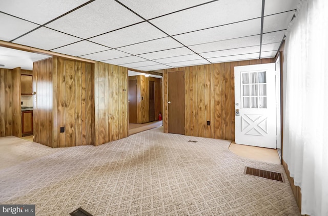 basement featuring wood walls, a paneled ceiling, and carpet flooring