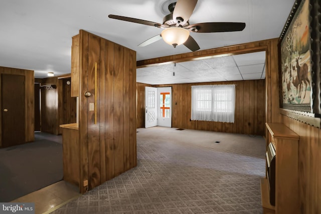 empty room featuring ceiling fan, wooden walls, and light carpet