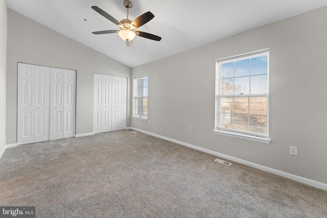 unfurnished bedroom with multiple closets, vaulted ceiling, and carpet