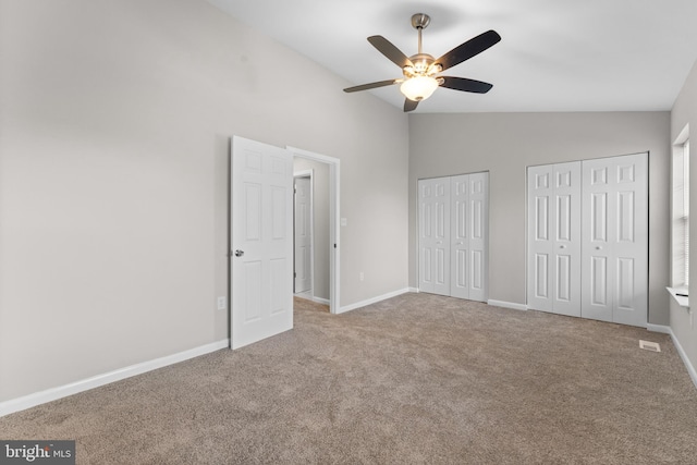 unfurnished bedroom featuring lofted ceiling, ceiling fan, two closets, and light carpet