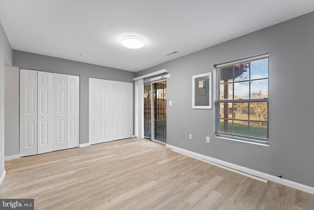 unfurnished bedroom featuring multiple closets and light hardwood / wood-style flooring