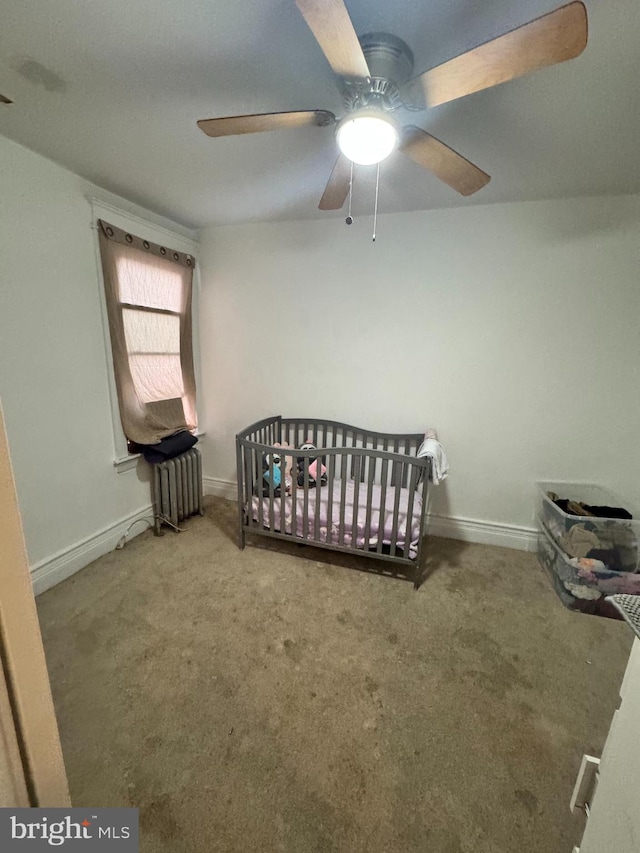 bedroom featuring a crib, carpet floors, ceiling fan, and radiator