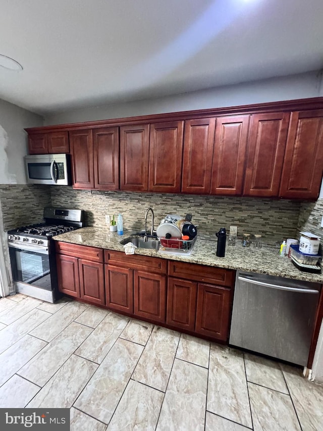 kitchen with backsplash, sink, light stone counters, and stainless steel appliances