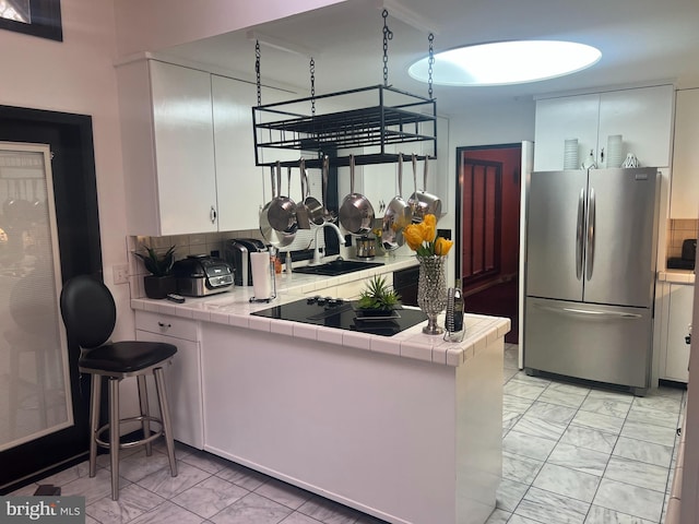 kitchen with black electric stovetop, white cabinetry, stainless steel refrigerator, decorative backsplash, and tile countertops