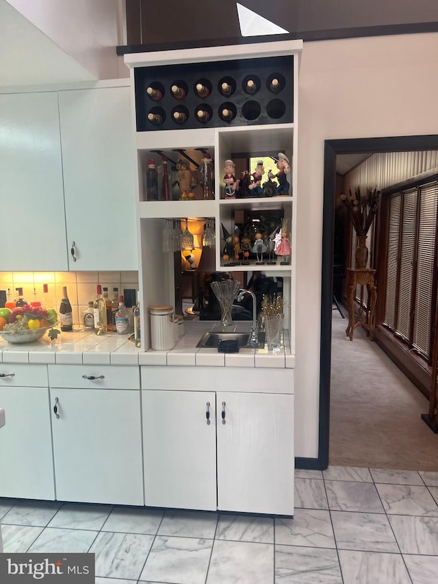 bar with tasteful backsplash, sink, light colored carpet, and tile counters