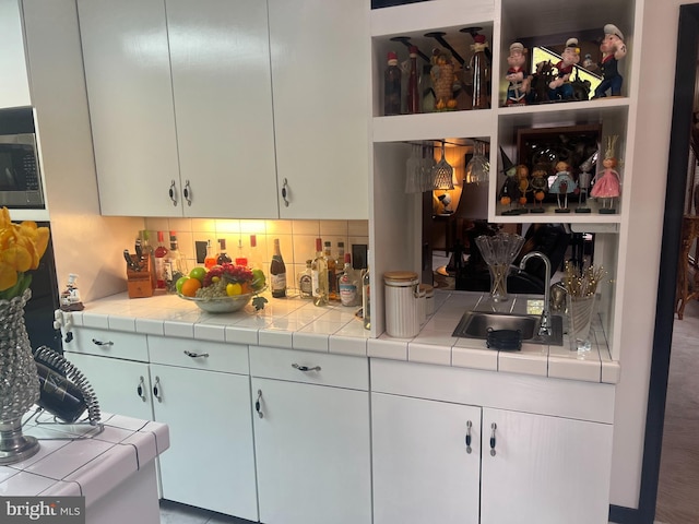 kitchen featuring white cabinetry, tile countertops, sink, and backsplash