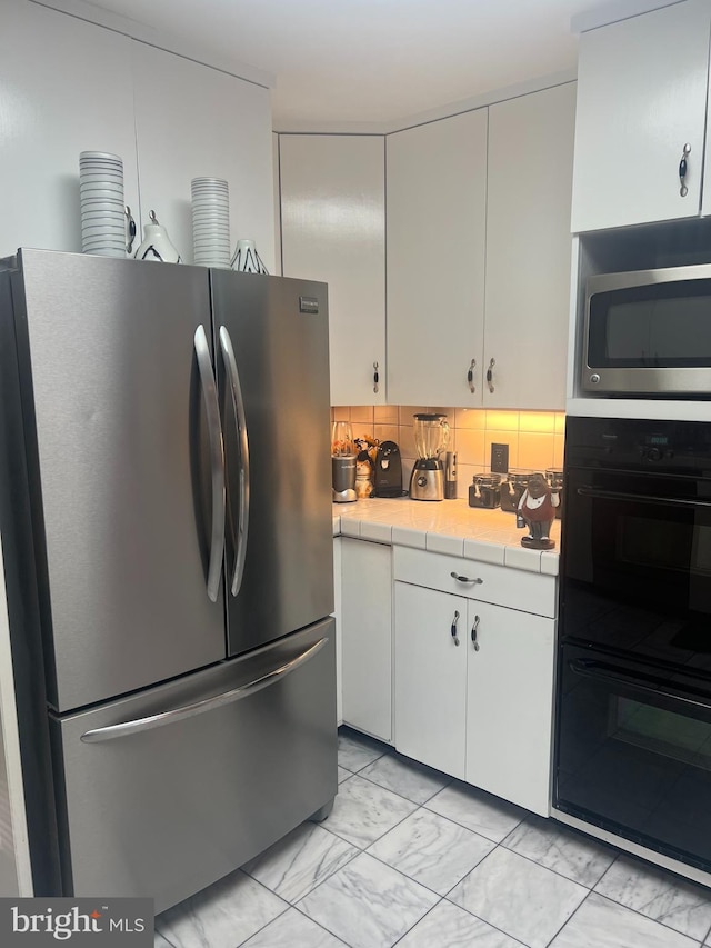 kitchen with white cabinets, decorative backsplash, appliances with stainless steel finishes, and tile counters