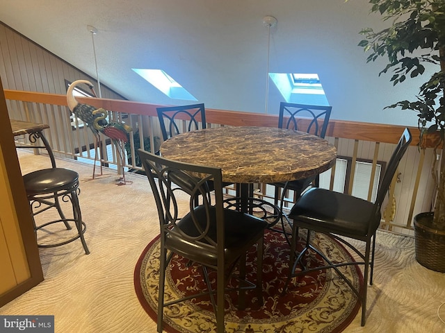 dining area featuring wooden walls, light carpet, and vaulted ceiling with skylight