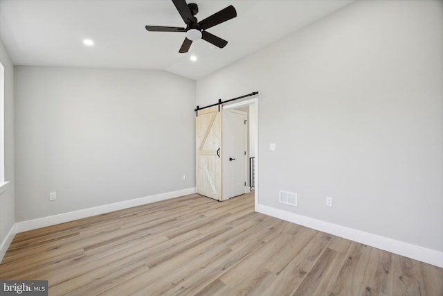 unfurnished bedroom with light hardwood / wood-style flooring, a barn door, ceiling fan, and vaulted ceiling