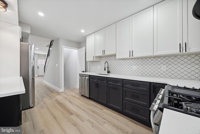 kitchen with white cabinetry, appliances with stainless steel finishes, decorative backsplash, sink, and light hardwood / wood-style floors