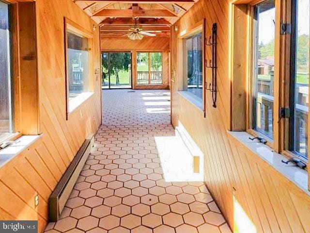 corridor featuring wood walls, beamed ceiling, and a baseboard heating unit