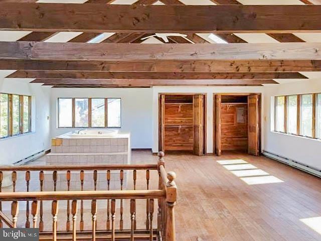 bedroom featuring hardwood / wood-style floors, beam ceiling, and a baseboard heating unit