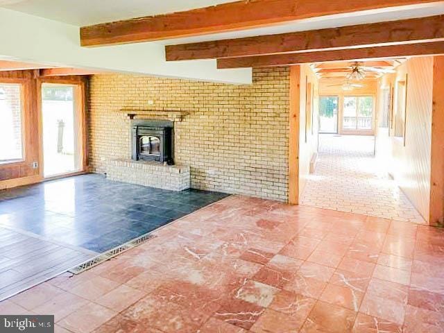 unfurnished living room with a wood stove, brick wall, ceiling fan, and beam ceiling