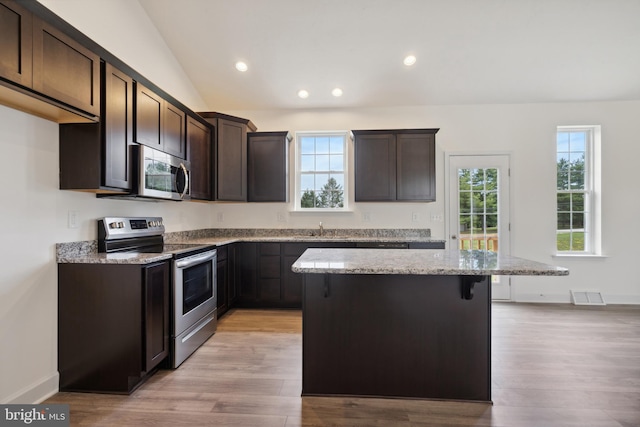 kitchen with stainless steel appliances, light hardwood / wood-style floors, light stone countertops, a kitchen island, and vaulted ceiling