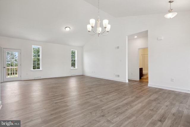 empty room with high vaulted ceiling, a notable chandelier, and hardwood / wood-style flooring