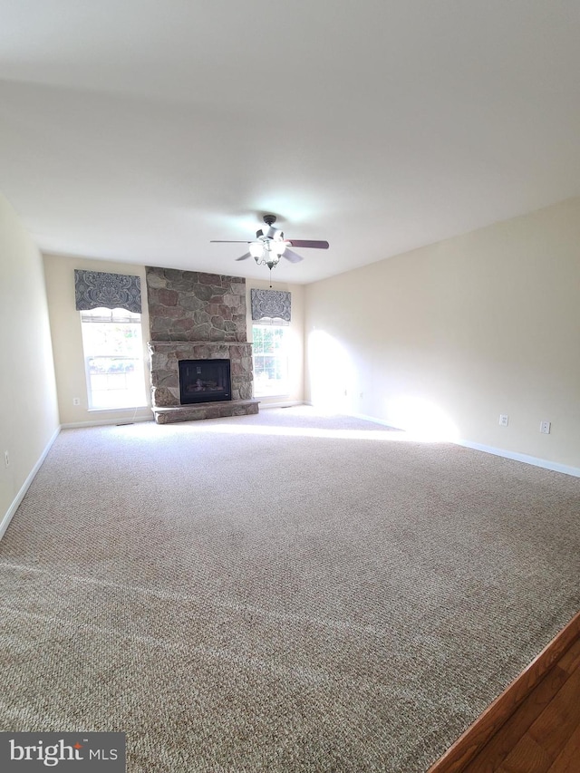 unfurnished living room featuring a stone fireplace, carpet, and ceiling fan