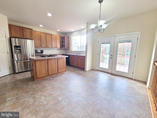 kitchen with stainless steel appliances, hanging light fixtures, a kitchen island, a notable chandelier, and decorative backsplash