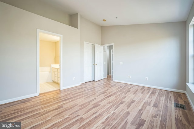 unfurnished bedroom featuring connected bathroom, high vaulted ceiling, and light hardwood / wood-style flooring