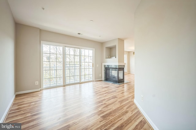 unfurnished living room featuring a multi sided fireplace and light wood-type flooring