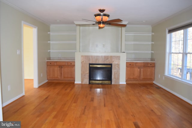 unfurnished living room with a premium fireplace, light wood-type flooring, ceiling fan, and ornamental molding