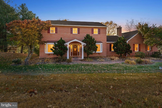 view of front facade with a chimney, a front lawn, and brick siding