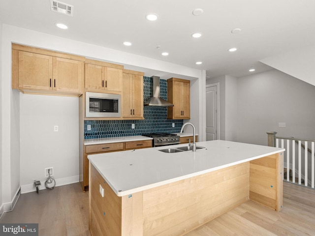 kitchen featuring wall chimney exhaust hood, light wood-type flooring, a kitchen island with sink, and appliances with stainless steel finishes