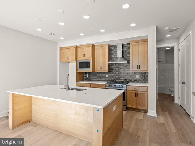 kitchen featuring appliances with stainless steel finishes, sink, an island with sink, and wall chimney range hood