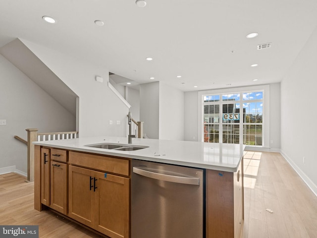 kitchen with stainless steel dishwasher, sink, light wood-type flooring, and an island with sink