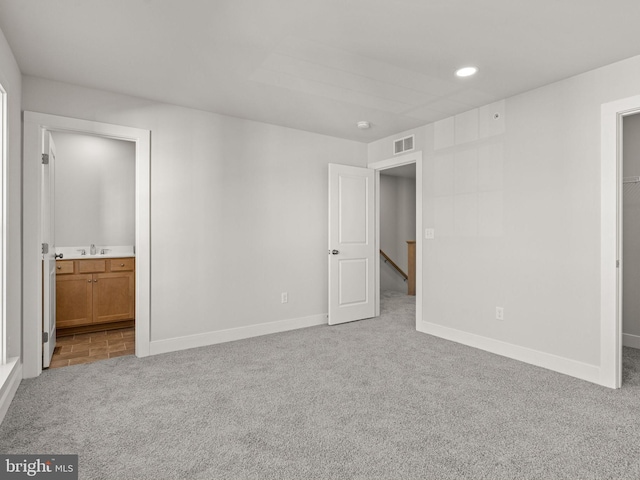 unfurnished bedroom featuring light carpet, ensuite bathroom, and sink