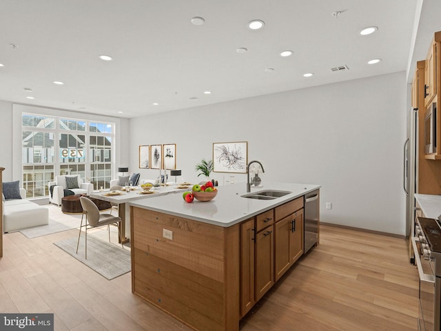 kitchen with light hardwood / wood-style flooring, sink, appliances with stainless steel finishes, and an island with sink