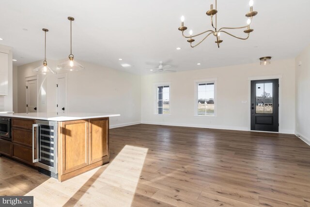 bar with ceiling fan with notable chandelier, beverage cooler, built in microwave, decorative light fixtures, and light hardwood / wood-style flooring